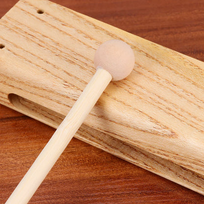 A light-colored madera dura wooden clapper and mallet with a foam head resting on a matching block una sola pieza