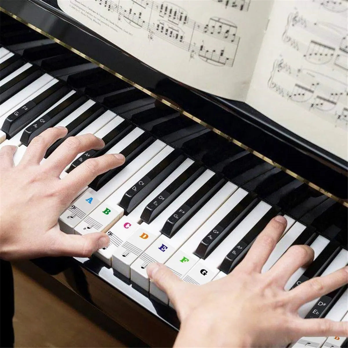 Hands playing a black and white electronic piano keyboard with colorful piano keyboard stickers and keyboard note stickers