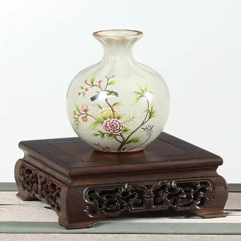 A delicate white porcelain vase with hand-painted floral and bird motifs displayed on a premium wooden pedestal