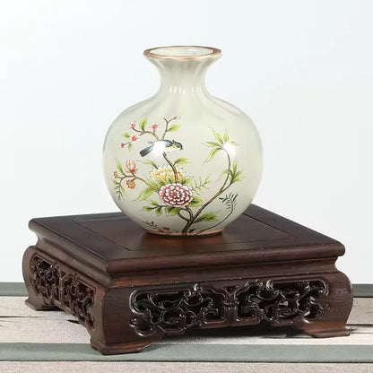 A delicate white porcelain vase with hand-painted floral and bird motifs displayed on a premium wooden pedestal