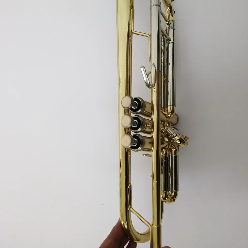 A shiny gold-plated brass professional bb trumpet with three valves and silver mouthpiece held against white background