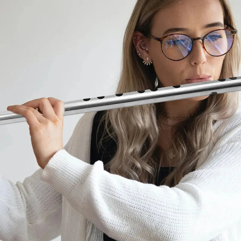 A silver stainless steel flute with black finger holes held by a person wearing glasses for music learners beginners