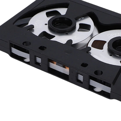 Black plastic blank cassette tape with silver metal spools and visible magnetic sound recording tape for music and speech