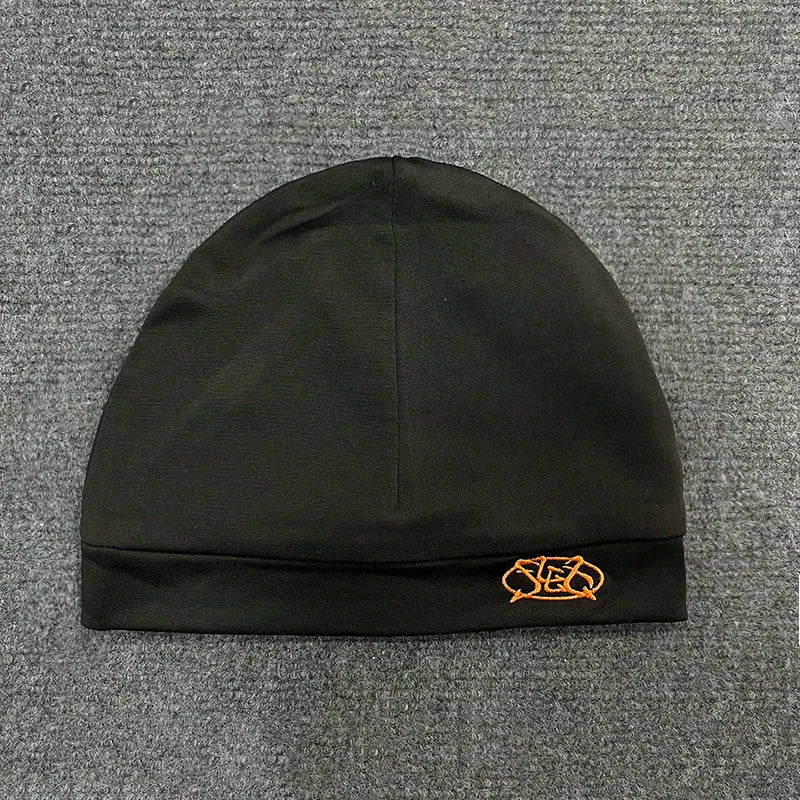Black knit pullover hat trendy with small orange embroidered letter cap on folded brim for fashionable streetwear