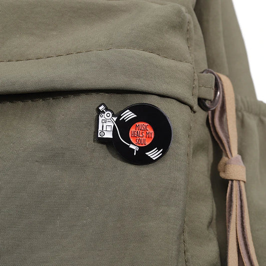 Black enamel retro music records pin featuring a white vinyl record player with orange center and music heals my soul text