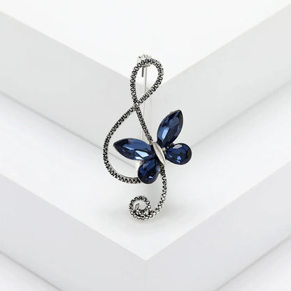 A navy blue rhinestone butterfly pin featuring a silver-toned shiny glass musical treble clef for event party backpack use