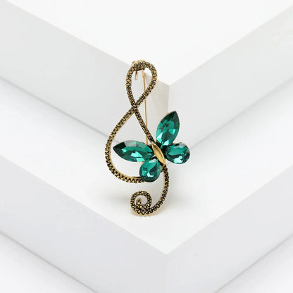 A sparkling emerald green rhinestone butterfly pin with gold-toned shiny glass musical treble clef for event party backpack decoration