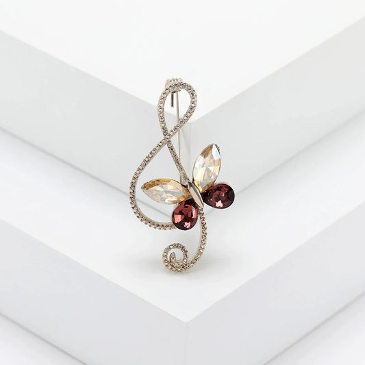 A sparkling silver rhinestone butterfly pin with amber and red gemstones on a shiny glass musical note for event party backpacks