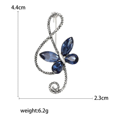 A sparkling silver rhinestone butterfly pin with deep blue gemstones and shiny glass musical note for event party backpack decoration