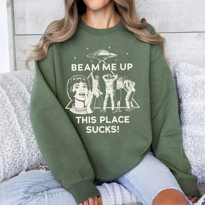 Olive green crewneck sweatshirt with white graphic of woman and five figures under text beam me up this place sucks man funny quote