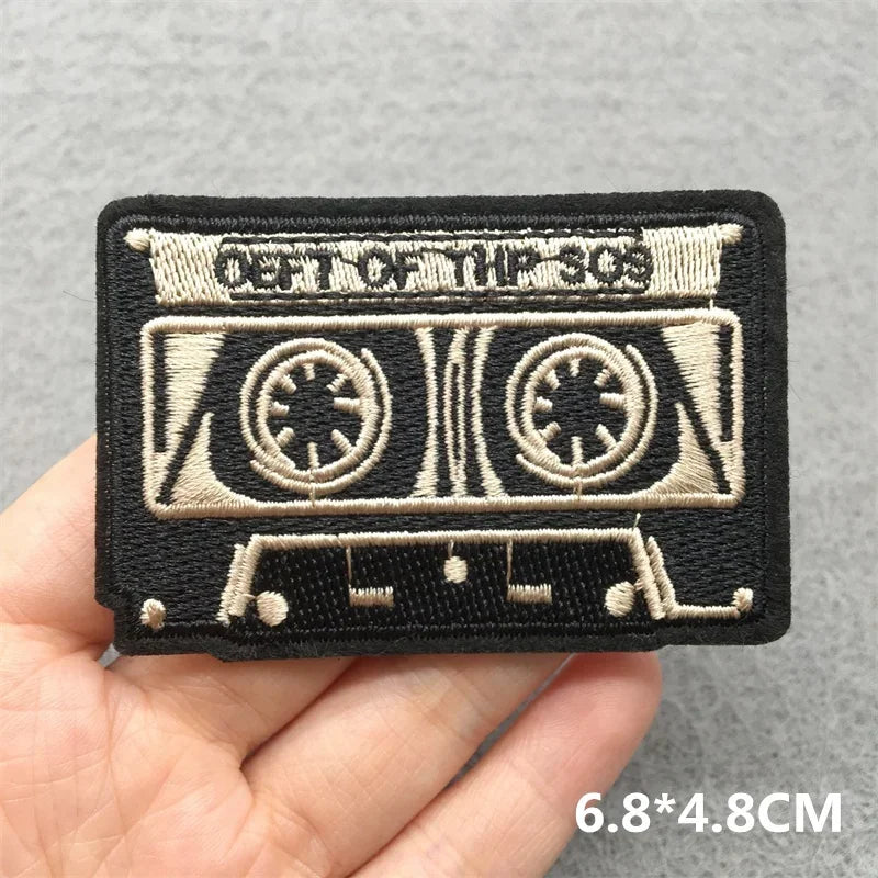 Black music embroidered patch shaped like cassette tape with beige stitching and out of the 80s text for jacket jeans headset