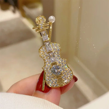 A sparkling gold violin-shaped brooch adorned with clear crystals and a pearl accent for women clothing decoration