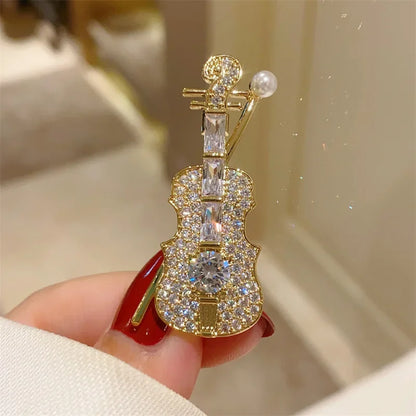 A sparkling gold violin-shaped brooch adorned with clear crystals and a pearl accent for women music accessories