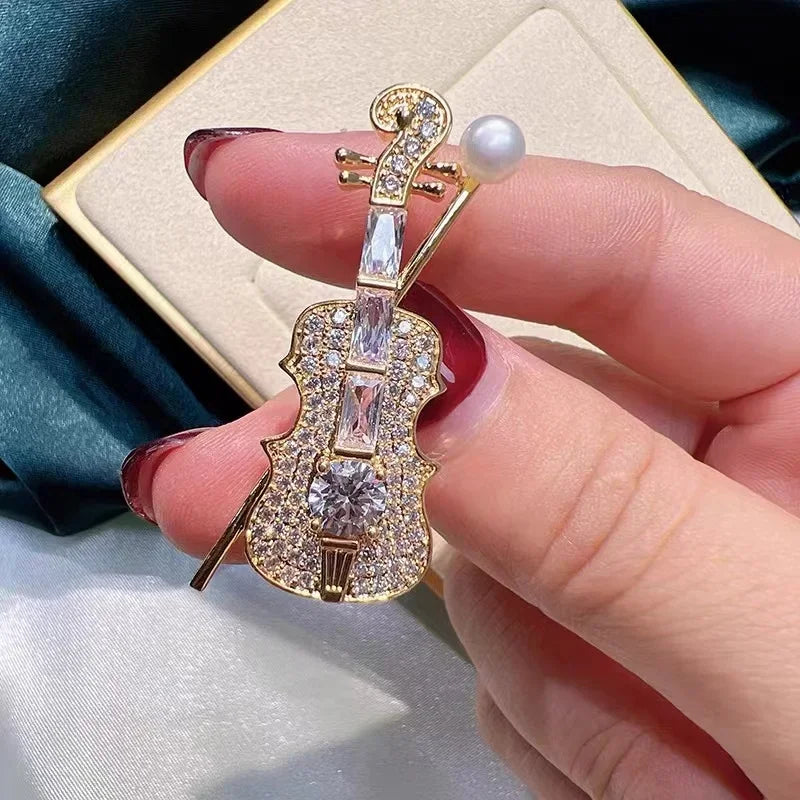 A sparkling gold violin-shaped brooch with clear crystals and a single pearl for women music accessory