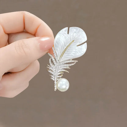 A delicate white mother-of-pearl feather brooch with rhinestones and a pearl for clothing decoration and music accessories