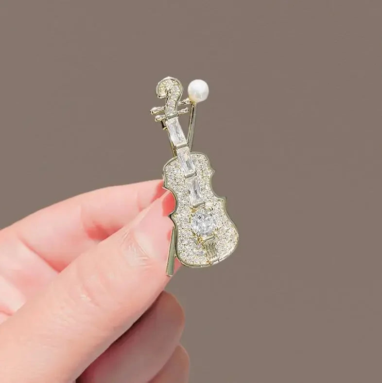 A sparkling silver violin-shaped brooch adorned with clear crystals and a pearl at the scroll for women