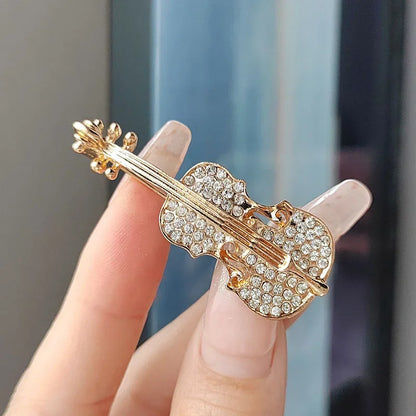 A gold-toned violin-shaped brooch adorned with sparkling clear crystals for clothing decoration