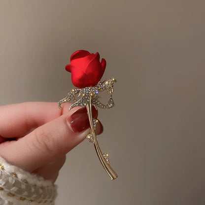 A red satin rose brooch with gold-toned stem and rhinestone leaves for women music accessory decoration