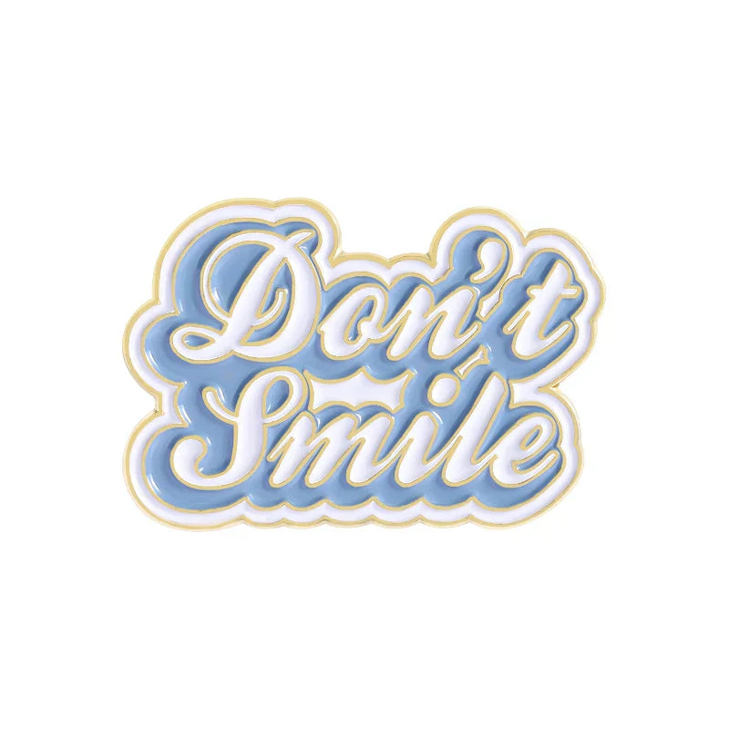 A light blue and white enamel pin with gold-trimmed cursive lettering don’t smile for sweet enamel pins and smile brooches clothes