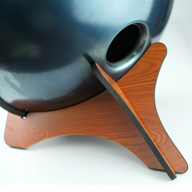 Dark blue metallic handpan resting on a solid wood drum stand for portable handpan storage and tongue drums display
