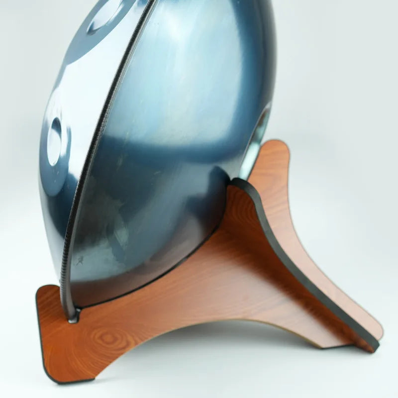 Shiny dark blue metallic handpan resting on a solid wood drum stand for portable handpan storage and tongue drums display