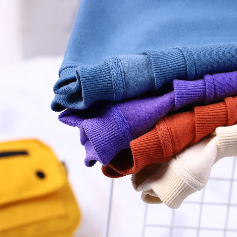 Stack of colorful knit sweaters in soft blue purple orange and cream hues complementing the loose fleece sweatshirt menswear fashion fitness hoodie crewneck