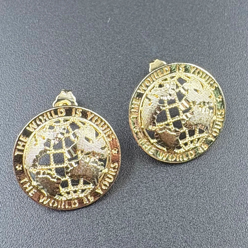 Gold-toned 14k gold plated stud earrings featuring an engraved globe and the phrase the world is yours hip hop style