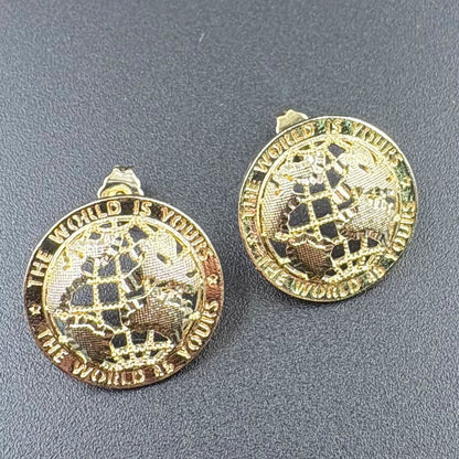 Gold-toned 14k gold plated stud earrings featuring an engraved globe and the phrase the world is yours hip hop style