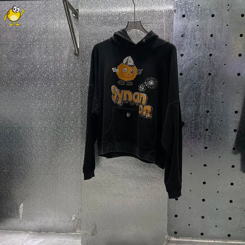 Black hoodie with cartoon pumpkin graphic and synan text hanging on a hanger in washed blue paly hoodies men style