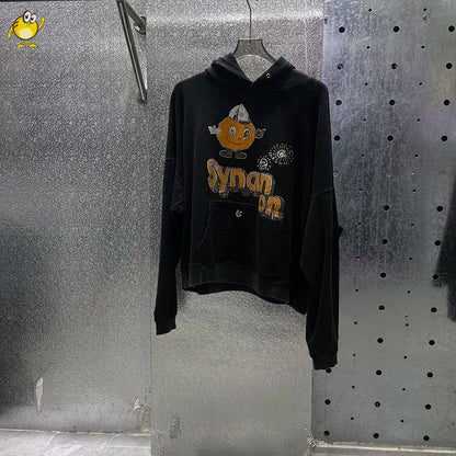 Black hoodie with cartoon pumpkin graphic and synan text hanging on a hanger in washed blue paly hoodies men style