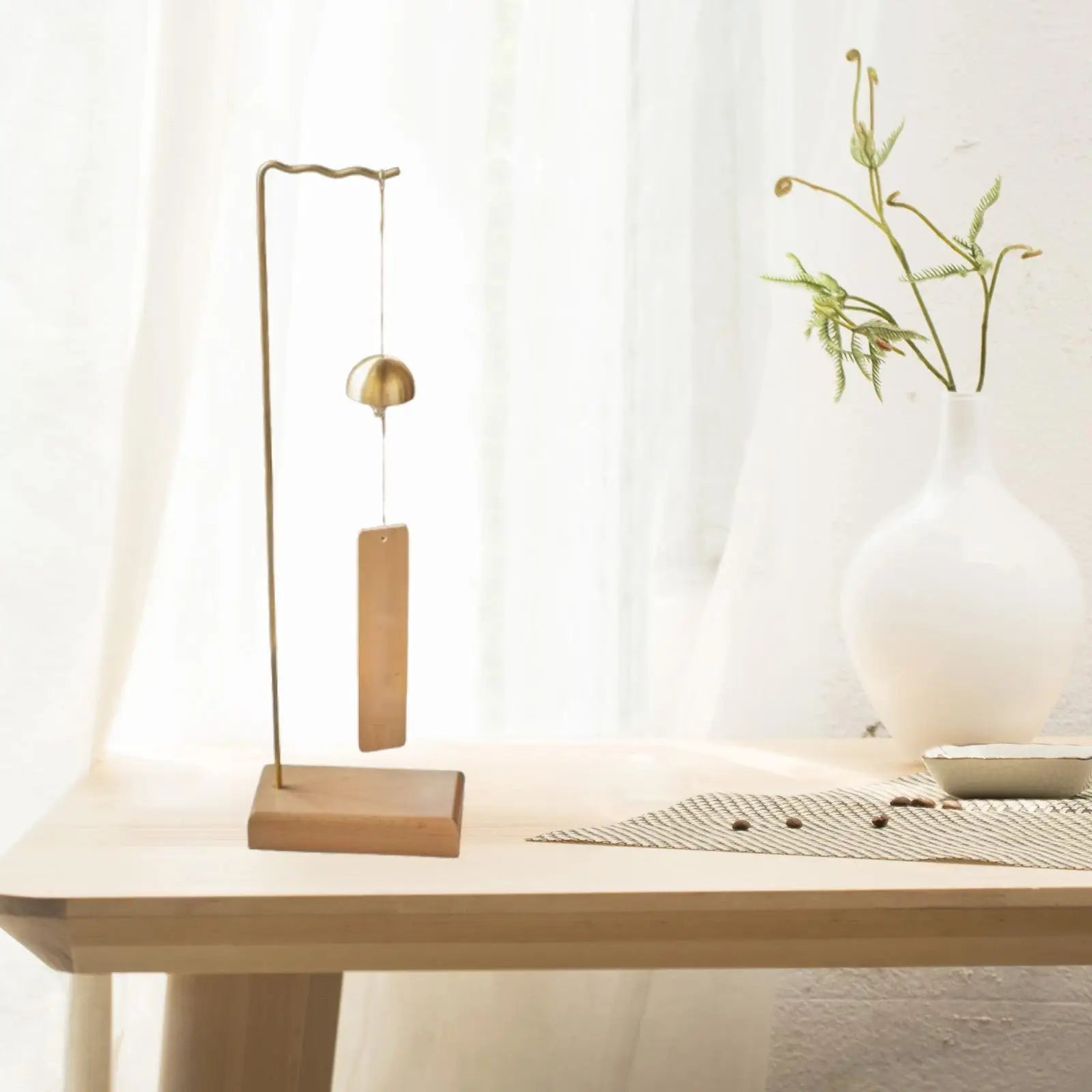 A minimalist brass pendulum clock with rectangular wooden base on a wind chime stand for wedding event home decor