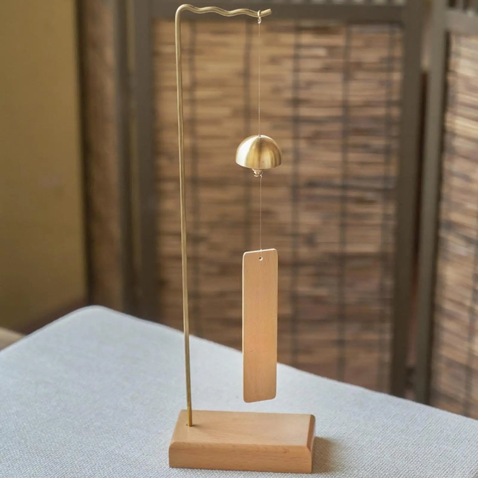 Minimalist brass wind chime with golden bell and wooden tag on a curved metal wind chime stand for wedding event home decor