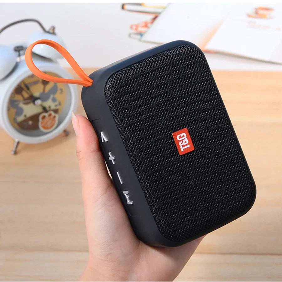 Black textured fabric wireless bluetooth speaker with orange carrying loop and red t&g logo featuring small subwoofer sound