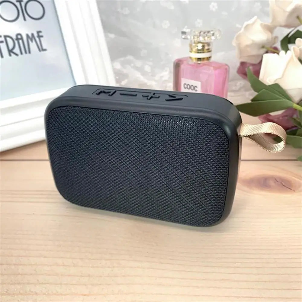Black rectangular wireless mini bluetooth speaker with textured fabric grille and beige strap designed for outdoor use