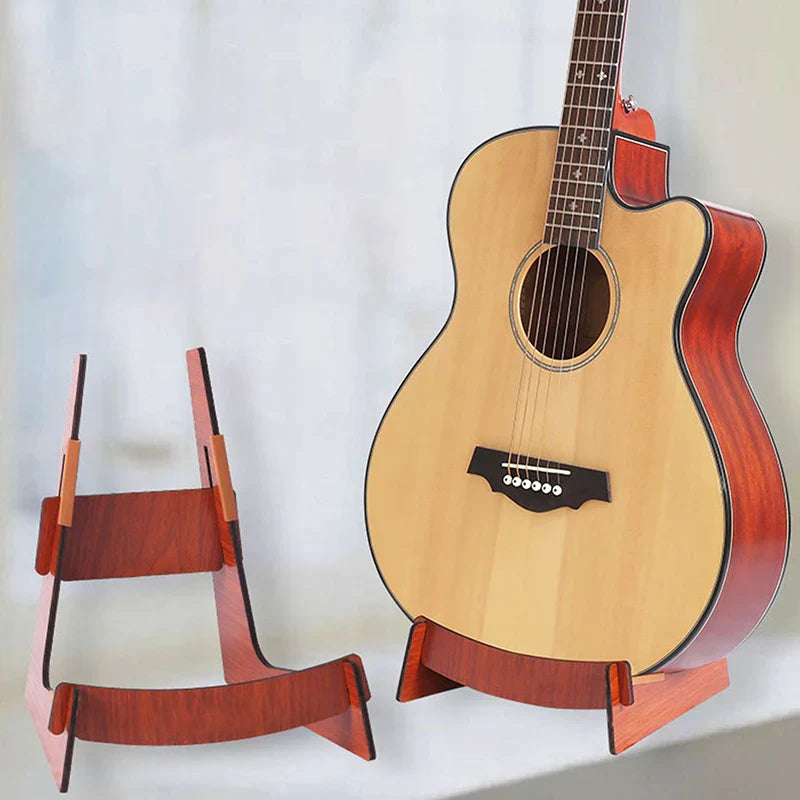 A light-colored acoustic guitar with glossy reddish-brown binding resting on a wooden guitar stand floor display holder