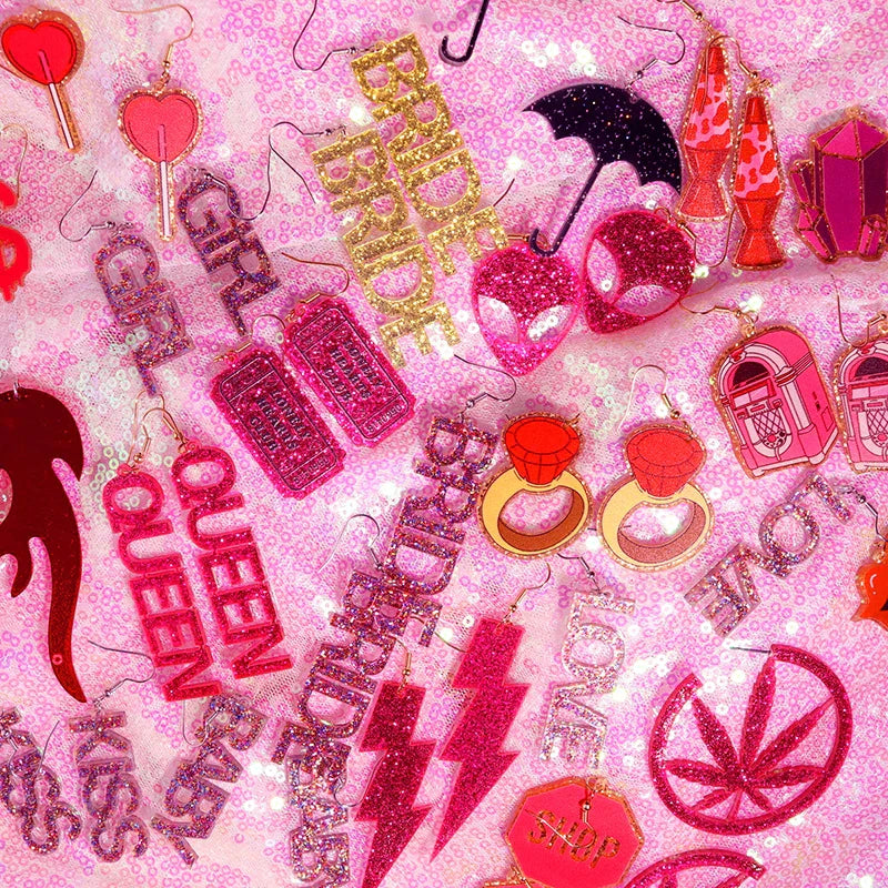 A collection of glittery pink and gold acrylic y2k earrings featuring cute flame snake, lightning queen alien, and playful designs