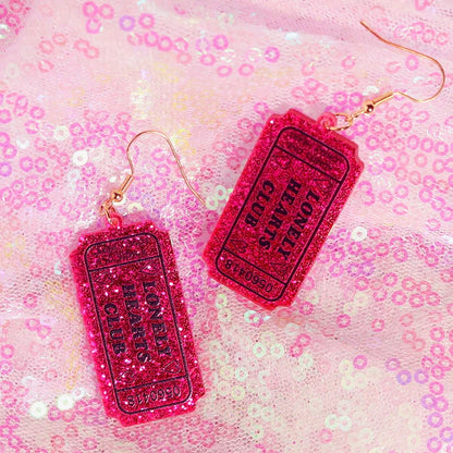 Vibrant pink glittery y2k earrings shaped like tickets with lonely hearts club text for cute flame snake and lightning queen alien style