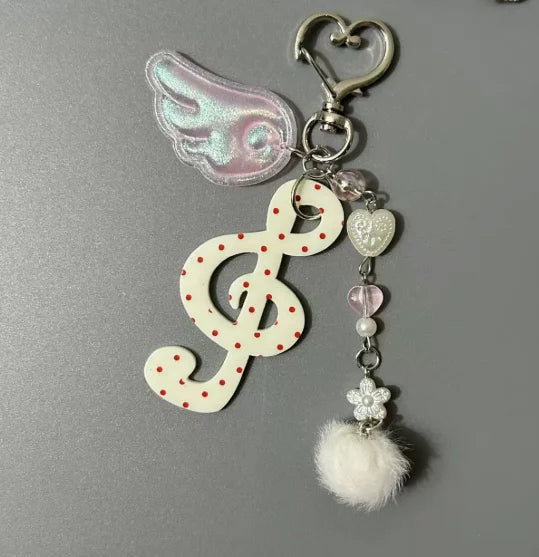 A y2k harajuku musical white treble clef keychain with red polka dots, pink wing charm, heart beads, pearls, and pom-pom