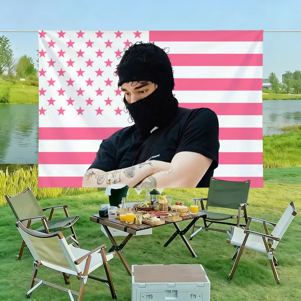 A man with tattoos wears a black beanie and mask in front of a pink and white american flag yeat singer a dangerous lyfe flag showing color difference