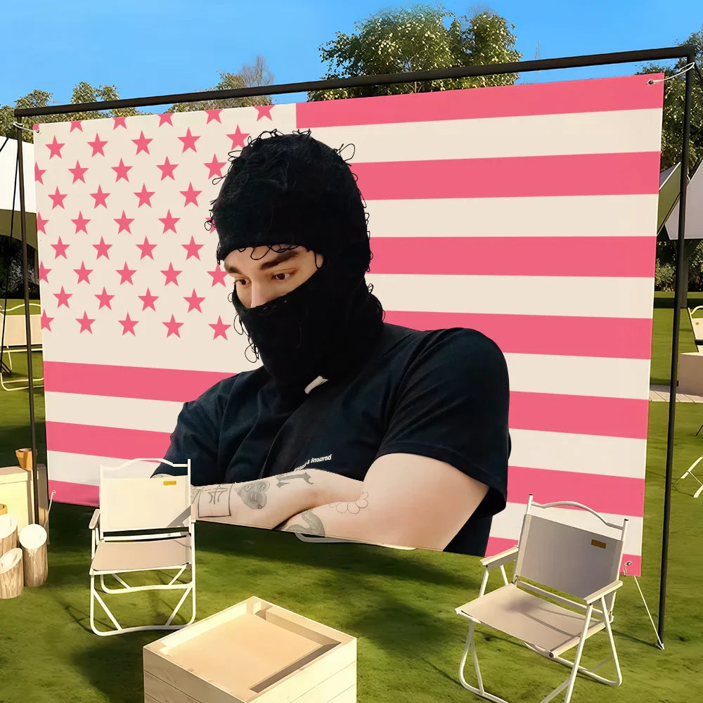 A person wearing a black balaclava stands before a pink and white striped yeat singer a dangerous lyfe flag showing color difference